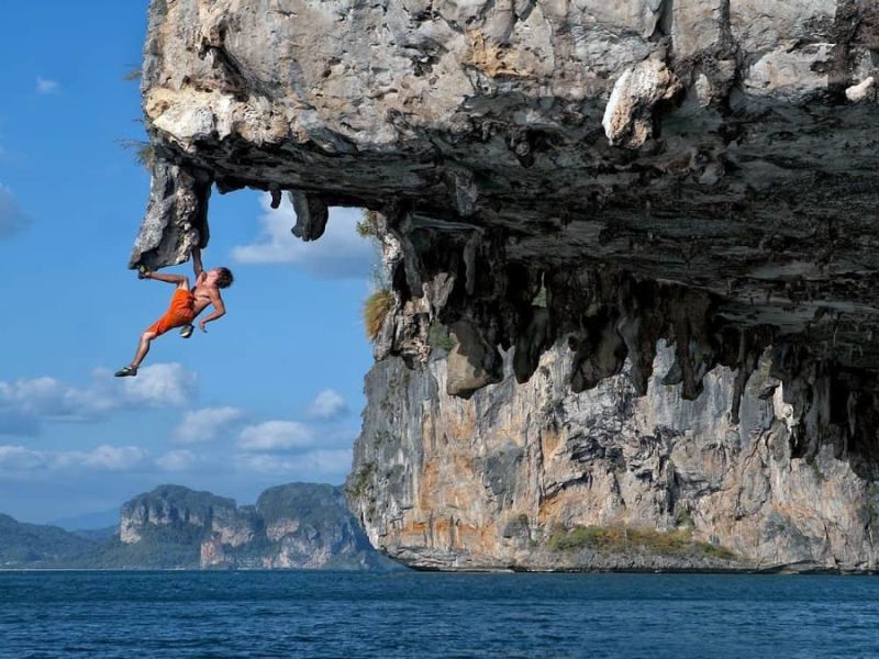A climber hanging from a heavily overhanging limestone roof directly above the sea