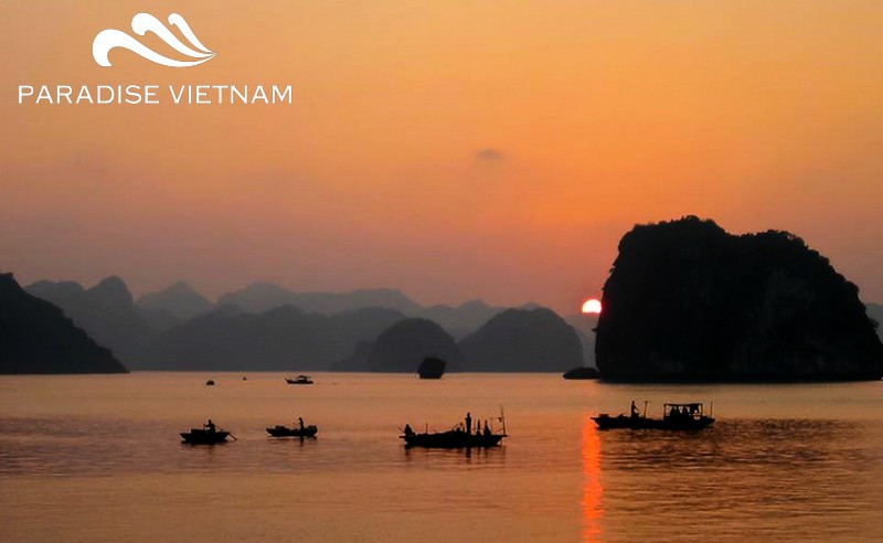 Low sun over Ha Long Bay with small fishing boats silhouetted on orange water