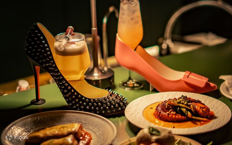 Two cocktails served in stiletto-shaped holders, one studded black and one pink, with small plates