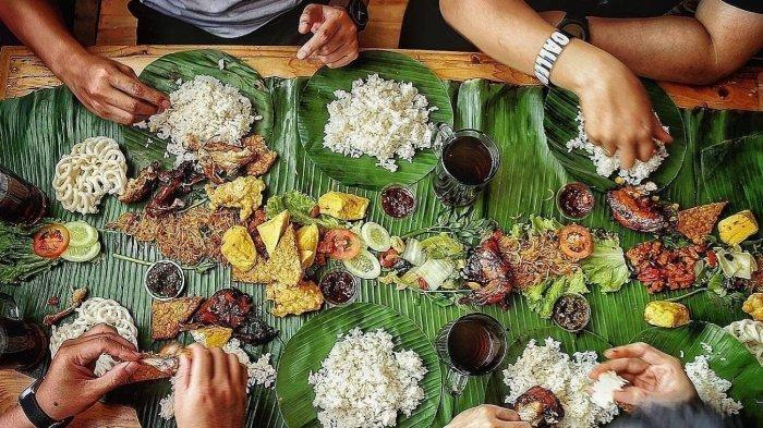 Diners reaching for rice, fried fish and vegetables spread along banana leaves on a table