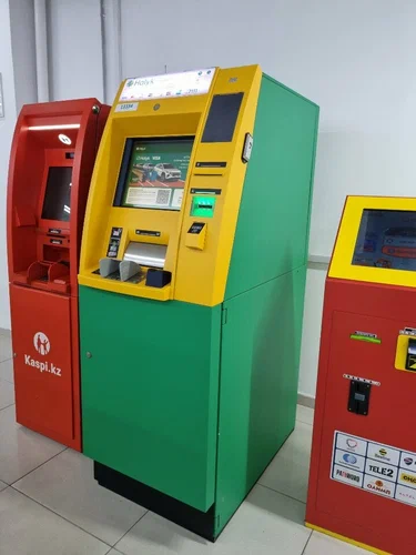 A red Kaspi.kz ATM beside a green and yellow bank ATM and a payment terminal