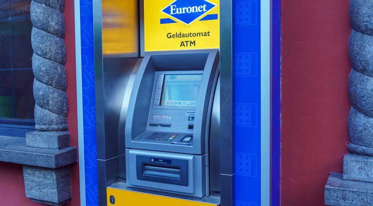 A blue and yellow Euronet cash machine mounted in a wall, signed Geldautomat ATM