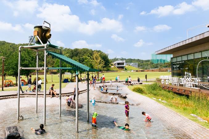 Children playing in a shallow paddling stream beside a tipping-bucket water frame