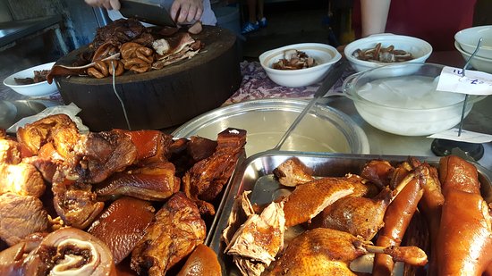 Trays of braised pork belly, trotters and offal beside bowls of broth at a kueh chap stall