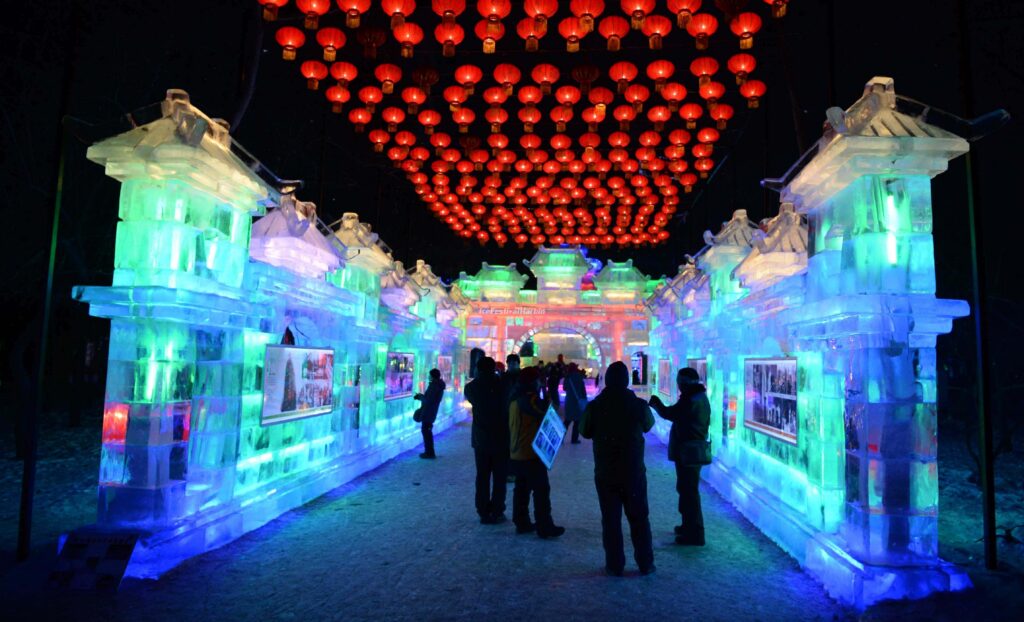Glowing ice archways lit blue and green under rows of red Chinese lanterns at Zhaolin Park
