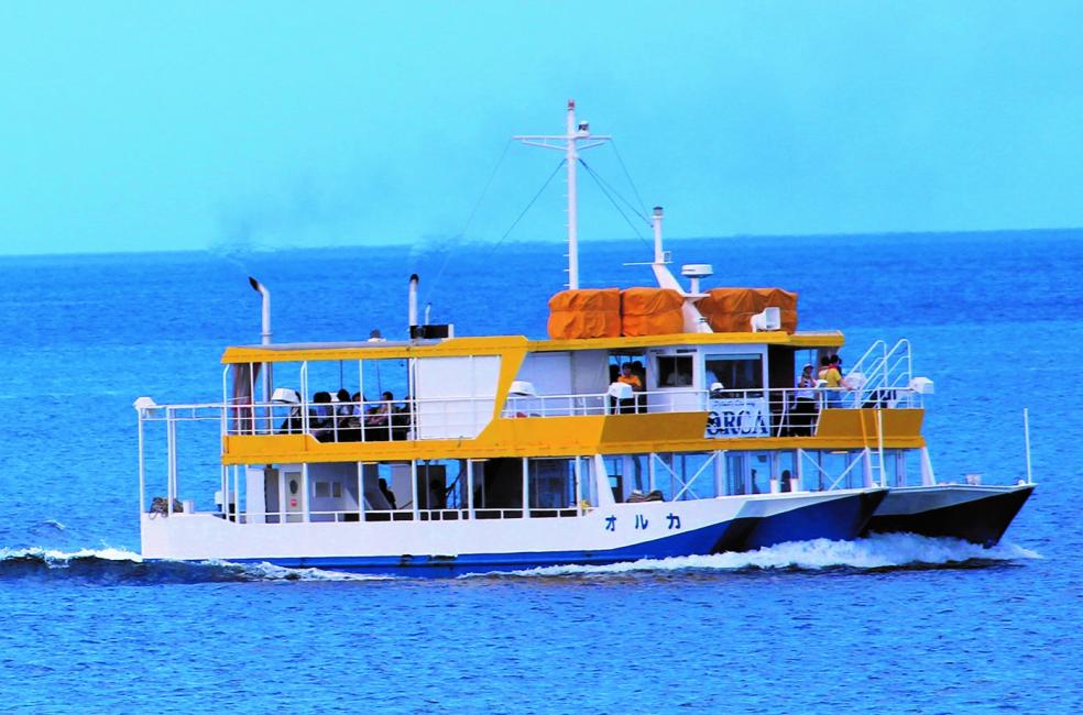 Small yellow and white passenger ferry crossing deep blue water with people on deck