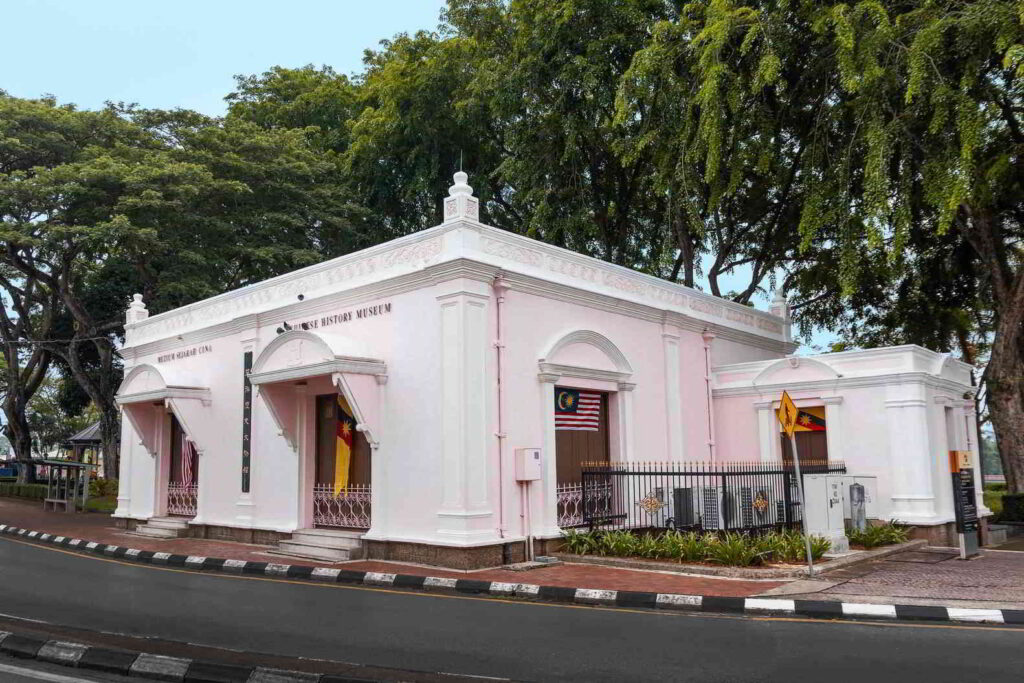 Pink single-storey colonial building signed Chinese History Museum beside a tree-lined road