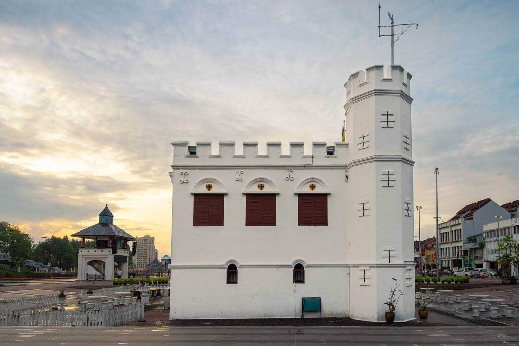 Whitewashed Square Tower with crenellated roofline and red shutters at dusk