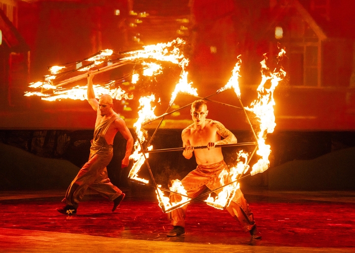 Two circus performers spin flaming props on a red-lit stage at Everland