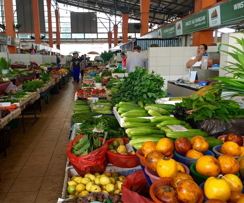 Market aisle stacked with jungle greens, cucumbers, dabai and citrus in coloured baskets