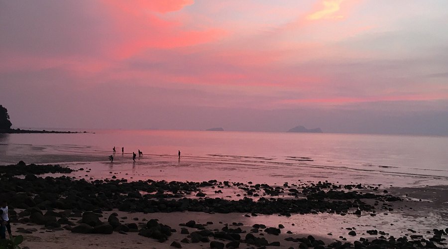 Pink and violet sunset over a rocky beach at low tide with figures on the wet sand