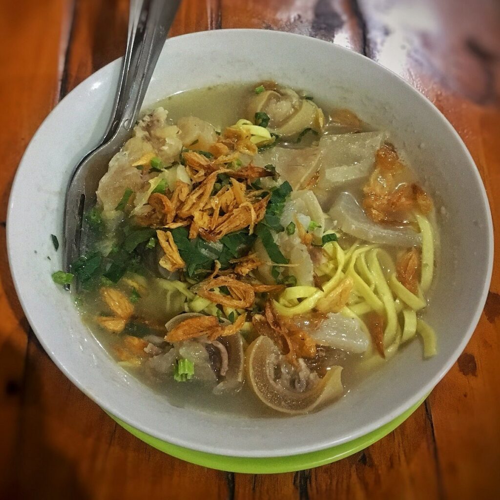Bowl of beef noodle soup with tendon, yellow noodles and fried shallots on a wooden table