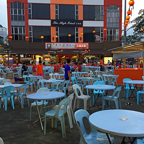 Rows of blue plastic tables under red lanterns at an open-air Kuching food court at dusk