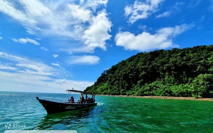 Small tour boat on turquoise water beside a steep forested island headland