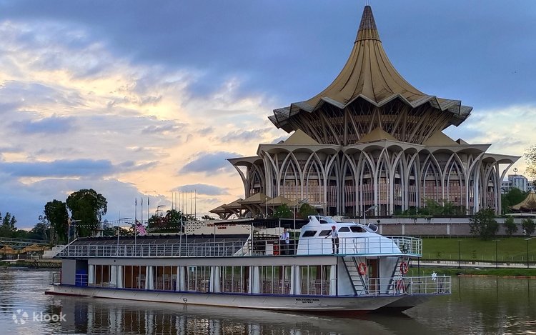 Double-deck cruise boat on the Sarawak River with the State Assembly building behind at dusk
