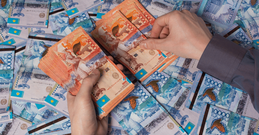 Hands counting a stack of 5,000 tenge notes above scattered 10,000 tenge banknotes