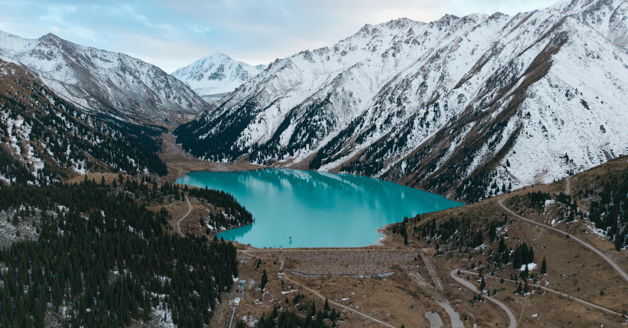Turquoise glacial lake below snow-covered peaks, with roads winding along the shoreline