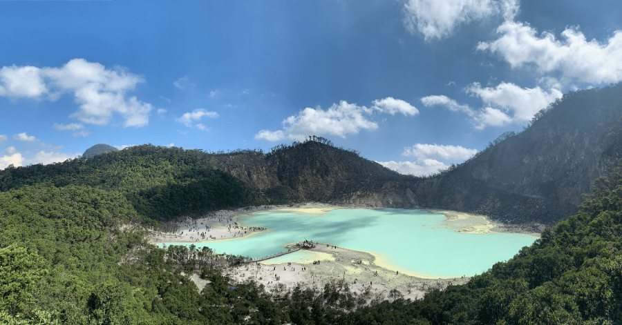 Turquoise crater lake at Kawah Putih ringed by pale sand and forested volcanic slopes