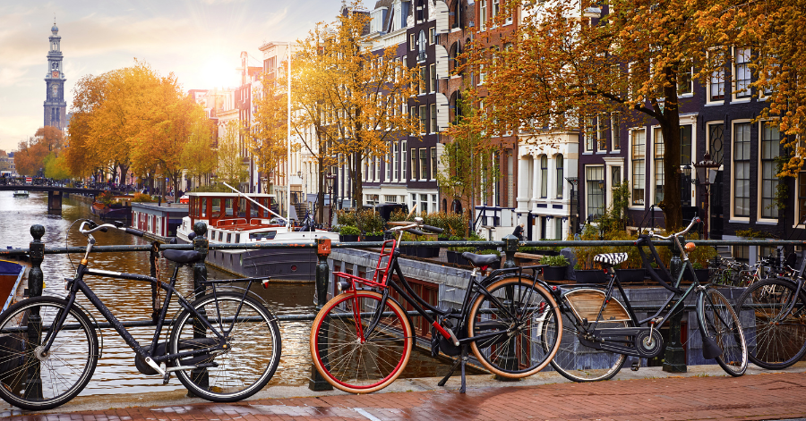 Bicycles chained to a canal railing in Amsterdam with autumn trees and a houseboat behind