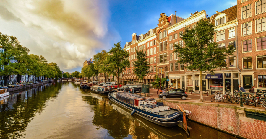 Houseboats moored along an Amsterdam canal lined with brick townhouses and parked bicycles