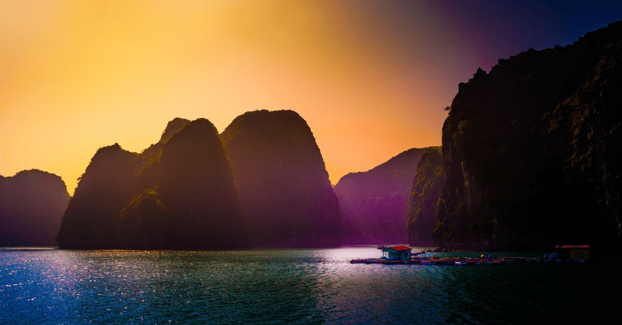 Gold and purple sunset over Ha Long Bay with a floating house on the water