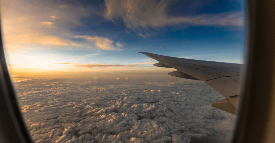 Aircraft wing above a thick cloud layer at sunset, seen from a passenger window