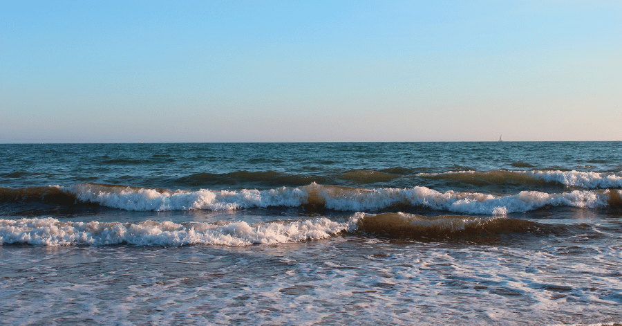 Small waves rolling onto a shallow shore under a pale evening sky