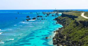 Clifftop road running out to a lighthouse on a green cape above turquoise reef water