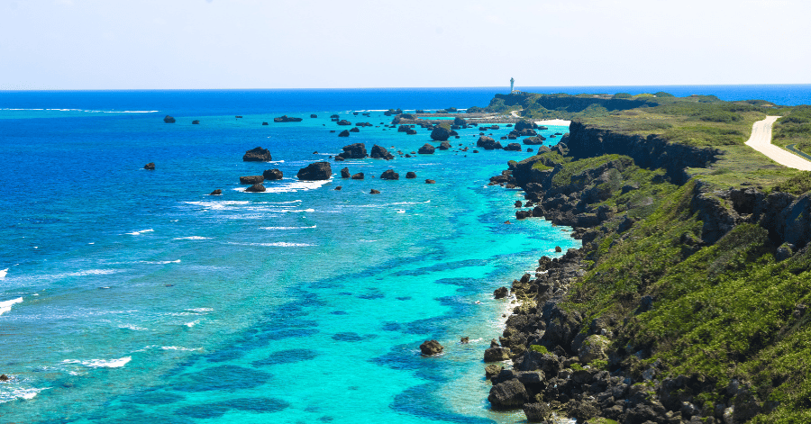 Clifftop road running out to a lighthouse on a green cape above turquoise reef water
