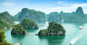 Forested limestone islands rising from turquoise water in Ha Long Bay, cruise boats threading between them