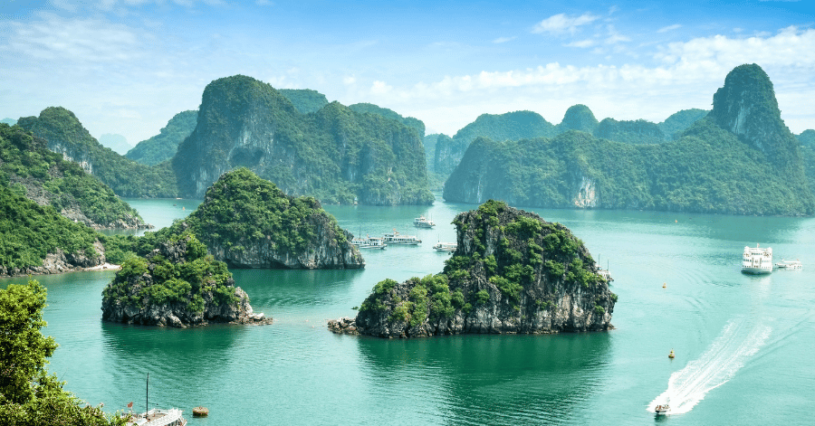 Forested limestone islands rising from turquoise water in Ha Long Bay, cruise boats threading between them