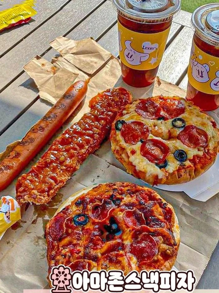 Two small pizzas, a corn dog and a sausage beside iced drinks in Lenny's cups