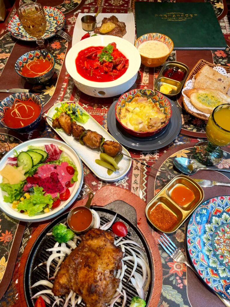 A table spread of Russian-Harbin dishes including borscht, bread, salad and a sizzling meat platter