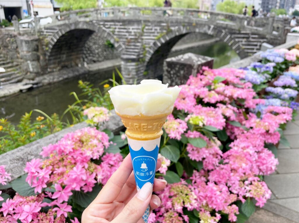 A rose-shaped Chirin ice cream cone held up in front of Meganebashi bridge
