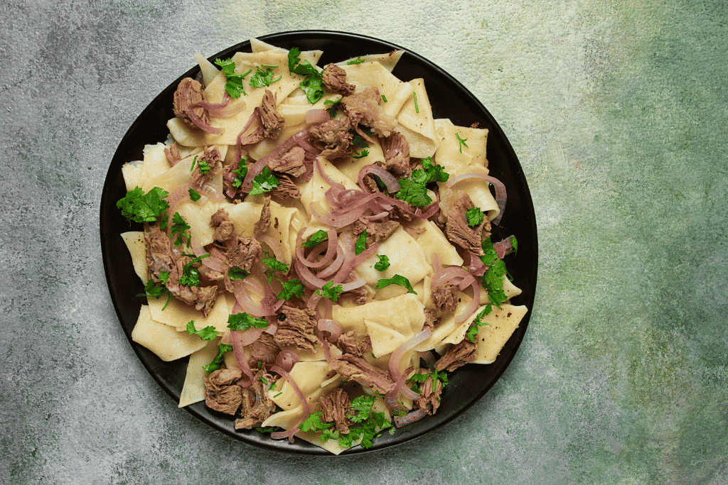 A plate of beshbarmak, boiled meat served over wide flat noodles with onion broth