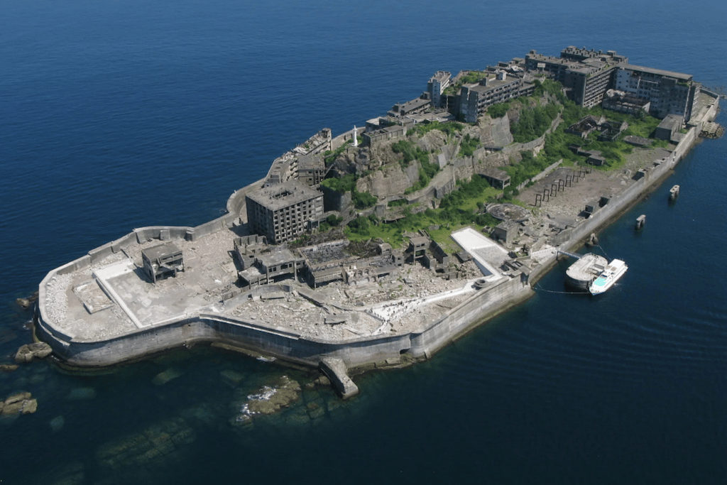 Aerial view of Gunkanjima's battleship-shaped seawall and ruined apartment blocks surrounded by sea