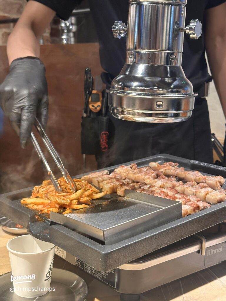 Staff grilling pork belly and kimchi on a griddle at Hanam BBQ