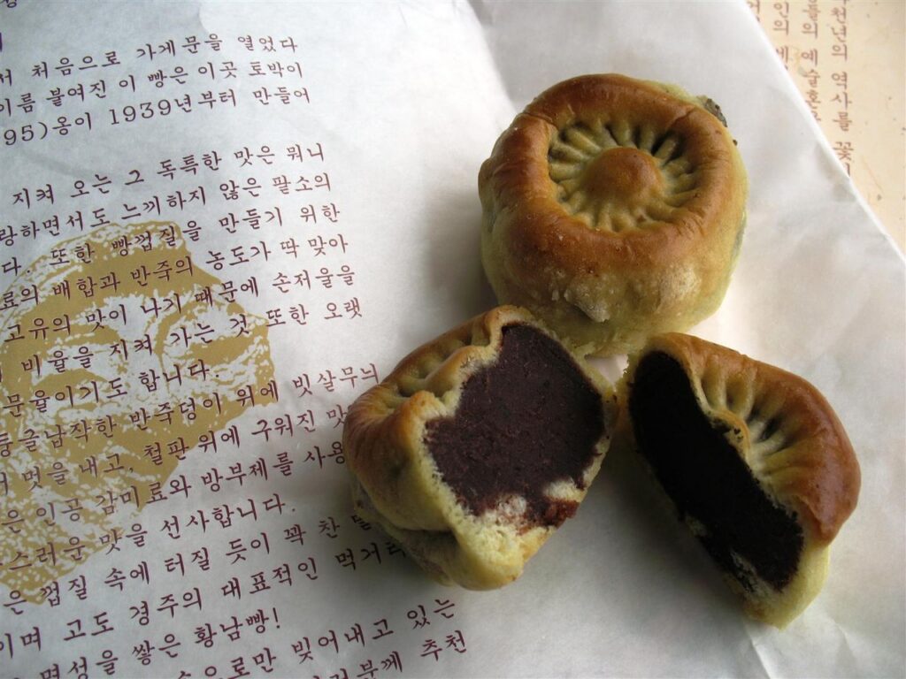 Hwangnam-ppang buns on printed paper, one split open to show the dense red bean filling