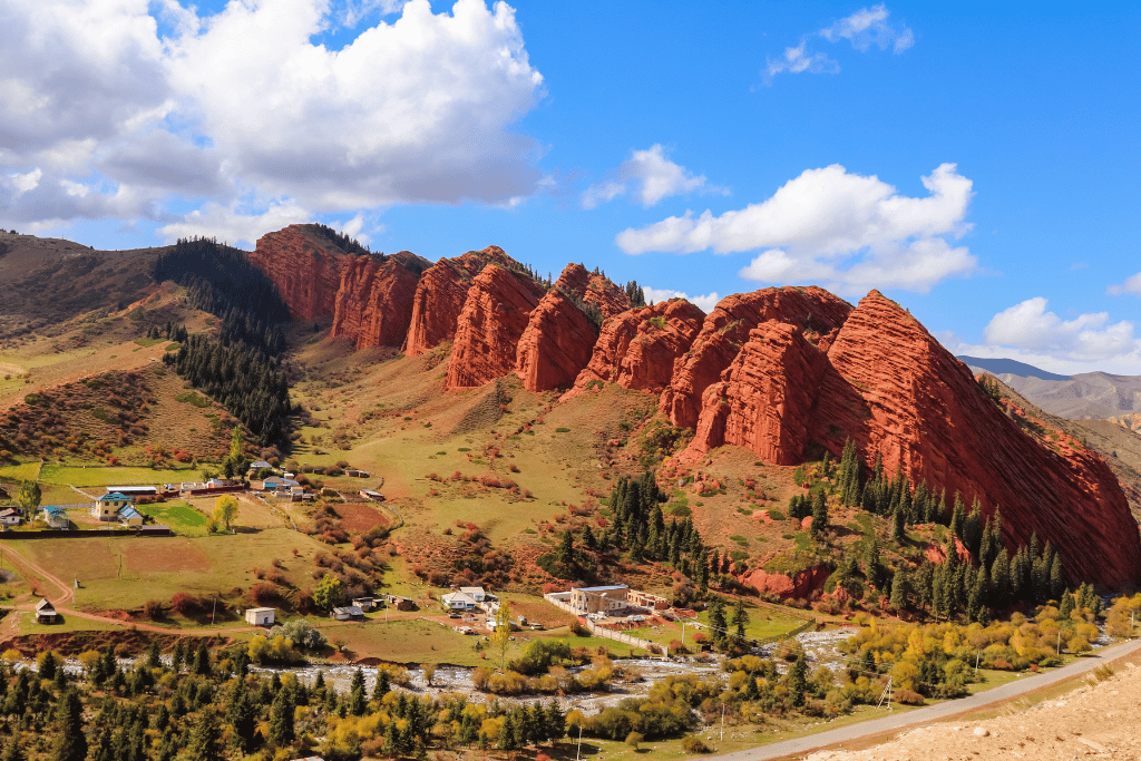 Red sandstone cliffs of Jeti-Ögüz Canyon rising above green pastureland