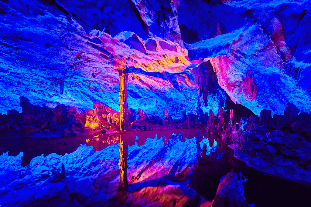 Illuminated stalactites in Reed Flute Cave, glowing blue, pink and orange
