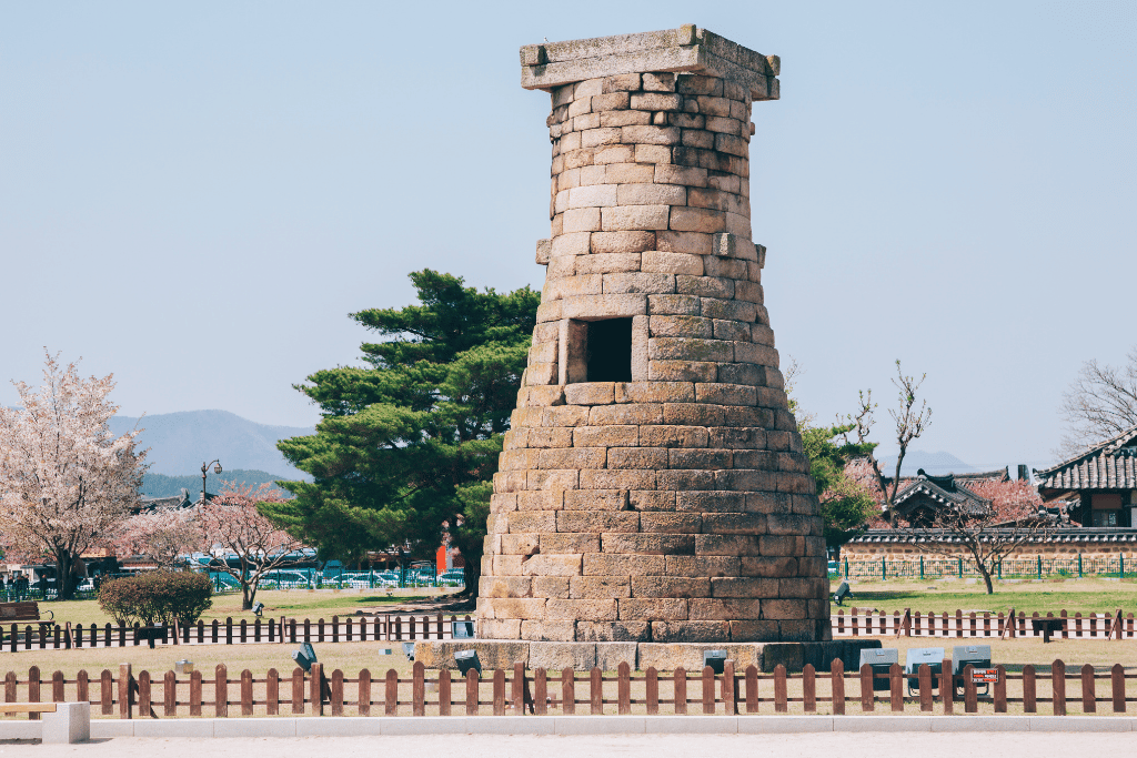 Cheomseongdae observatory, a bottle-shaped granite tower, with cherry blossom in the park behind