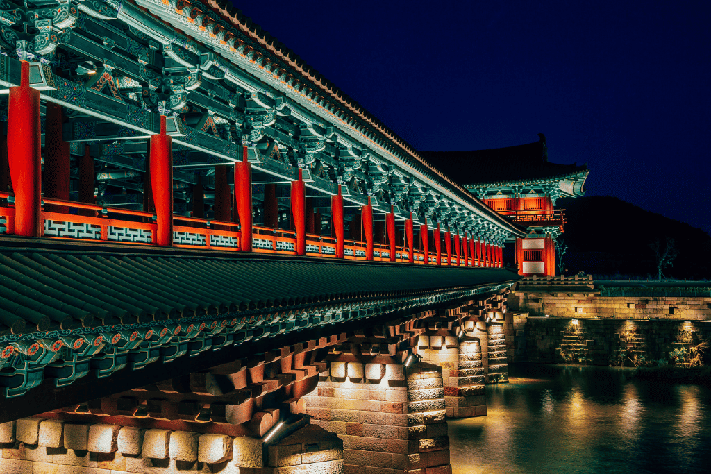 Woljeonggyo Bridge lit at night, red pillars and painted eaves above its stone piers
