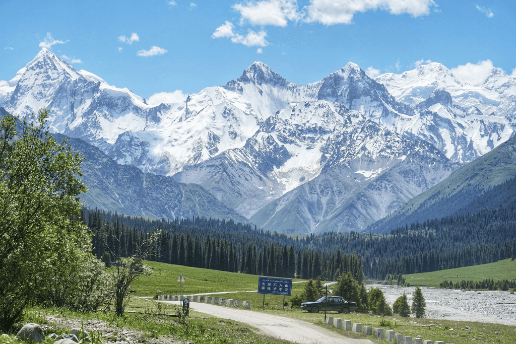Snow-capped Tian Shan mountain range towering over a valley road and forest