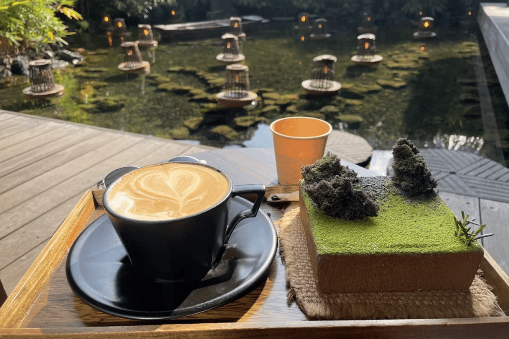 Latte and a matcha cake on a wooden tray beside Cheongsudang's lantern-dotted water garden