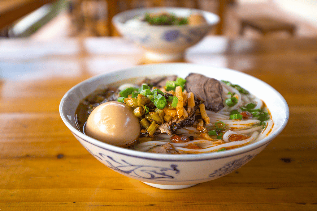 A bowl of Guilin rice noodles topped with a braised egg, sliced meat and spring onion