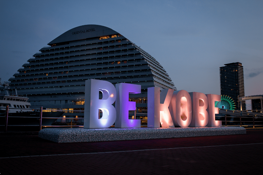 The illuminated BE KOBE sign in Meriken Park at dusk with the Kobe Meriken Park Oriental Hotel behind