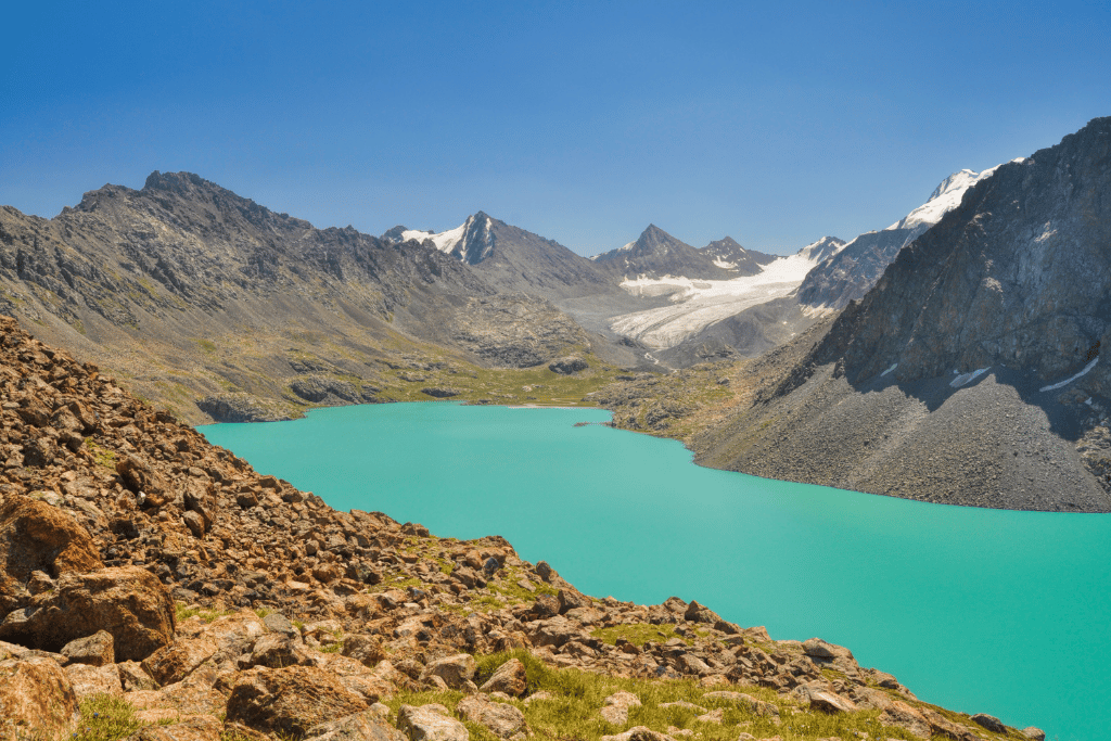 A turquoise alpine lake surrounded by rocky, snow-dusted Tian Shan peaks