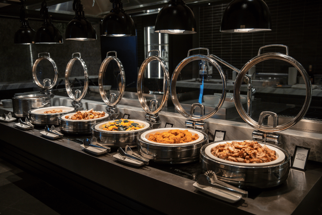 Hotel buffet counter with open chafing dishes of curry, fried chicken, and vegetables