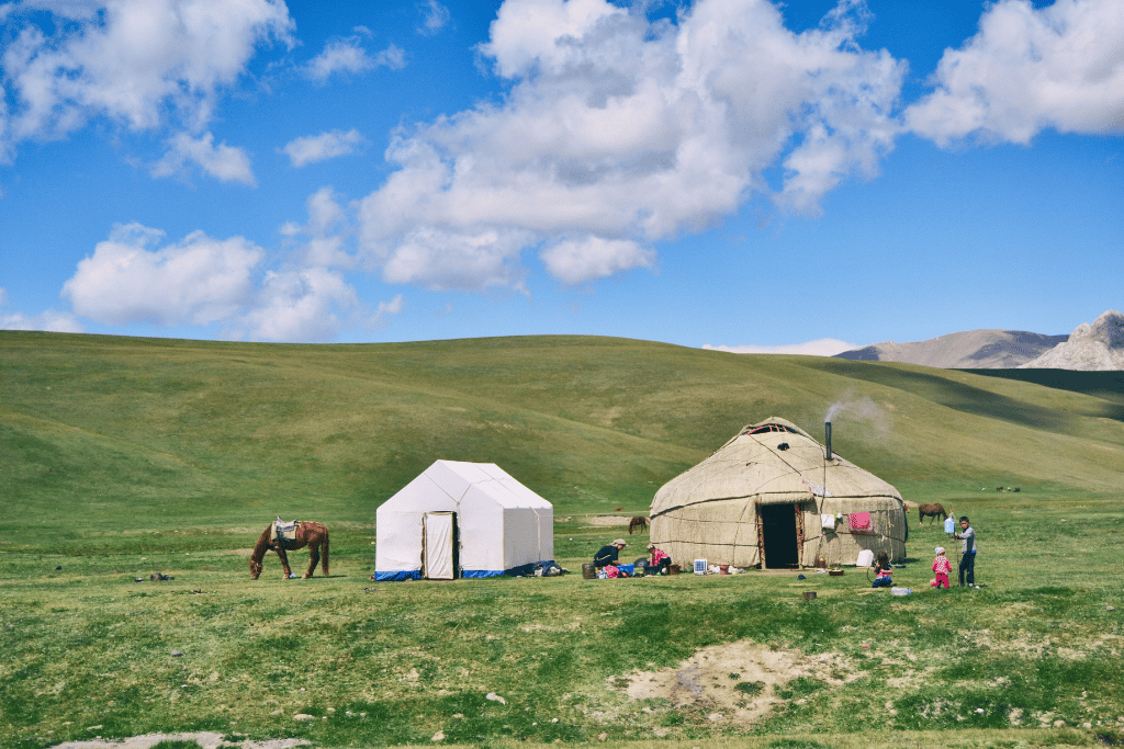 A family's yurt camp on open grassland, with a horse grazing and smoke rising from the yurt