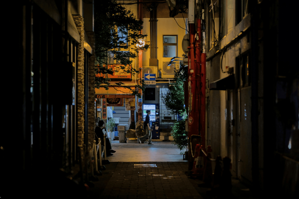 A narrow lit-up backstreet alley in Japan at night with a passerby